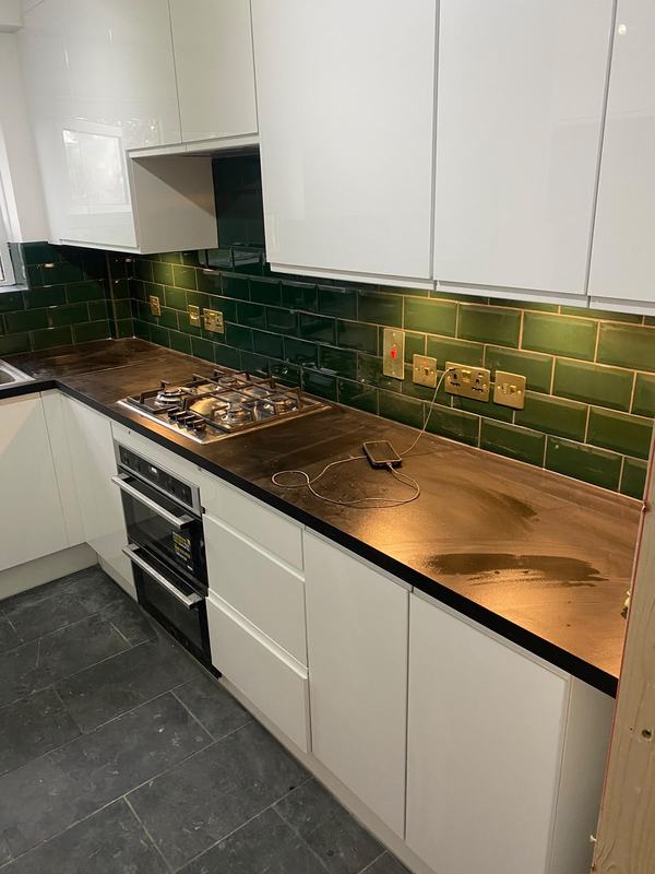 Kitchen with white cabinets and green tile splashback
